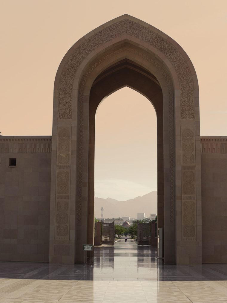 A carved stone arch at the Sultan Qaboos Grand Mosque in Muscat, mountains beyond